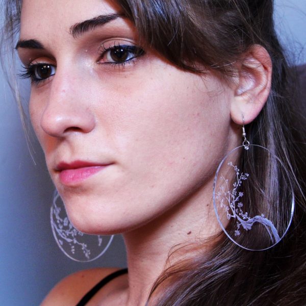 Fille avec des boucle d'oreille en plexiglas transparent gravé à la main de branche de cerisiers